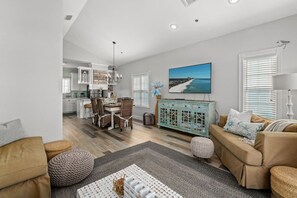 A modern living room with a dining area, a teal cabinet, and a beach-themed painting.