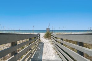 A wooden boardwalk leading to a beach with clear skies.