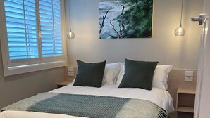 A neatly made bed with a white and green bedspread, two dark pillows, and a painting of trees on the wall. - Tinakori Village Retreat - 
Renovated apartment in a charming heritage building (Wellington)