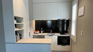 A modern kitchen with white cabinets, a black backsplash, and a built-in oven. - Tinakori Village Retreat - 
Renovated apartment in a charming heritage building (Wellington)