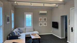 A compact living space with a sofa, a coffee table, a TV, and a door leading to another room. - Tinakori Village Retreat - 
Renovated apartment in a charming heritage building (Wellington)
