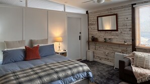 Une chambre à coucher comprenant un lit, une table de chevet, une commode, un miroir, un radiateur et une fenêtre avec des stores.