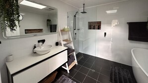 Une salle de bain moderne avec un grand miroir, un meuble-lavabo blanc, un sol carrelé noir, une douche en verre et une serviette noire accrochée au mur.