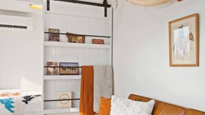 A modern bedroom with a bed, a sofa, a wall-mounted shelf with decorative items, and a framed picture on the wall. - Cowboy Shipping Container With Private Hot Tub (Columbia Falls)