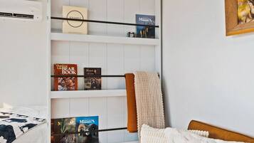 A bedroom with a white bed, a shelf with books, a blanket, and a framed picture on the wall.