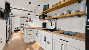 A modern kitchen with white cabinets, a wooden countertop, and a black sink. There are hanging pendant lights and a shelf with jars. - Romantic Container Near Glacier w/ Private Hot Tub (Columbia Falls)