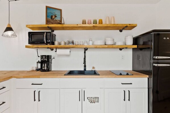 A kitchen with white cabinets, a wooden countertop, a black microwave, a coffee maker, and a refrigerator.