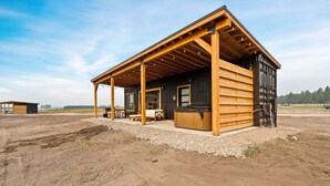 A wooden cabin with a covered porch, a hot tub, and a small outdoor seating area. - Romantic Container Near Glacier w/ Private Hot Tub (Columbia Falls)