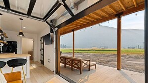 A modern kitchen with a dining area, a bench, and a view of a rural landscape. - Romantic Container Near Glacier w/ Private Hot Tub (Columbia Falls)