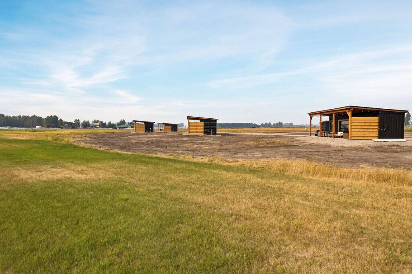 A rural setting with three wooden cabins and a larger building with a porch.