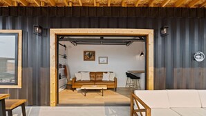 A cozy living room with a brown leather sofa, a wooden coffee table, and a white couch. There is a small dining area with a wooden table and two chairs. The room has a wooden ceiling and walls with a black and white color scheme. - Romantic Container Near Glacier w/ Private Hot Tub (Columbia Falls)