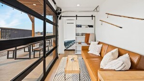 Et moderne interiør med et stort vindue, en træbænk udenfor og en brun lædersofa med puder.