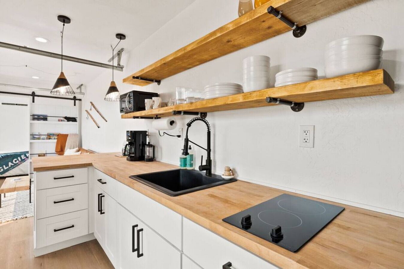 Une cuisine moderne avec des meubles blancs, un plan de travail noir et des étagères en bois au-dessus de l’évier.