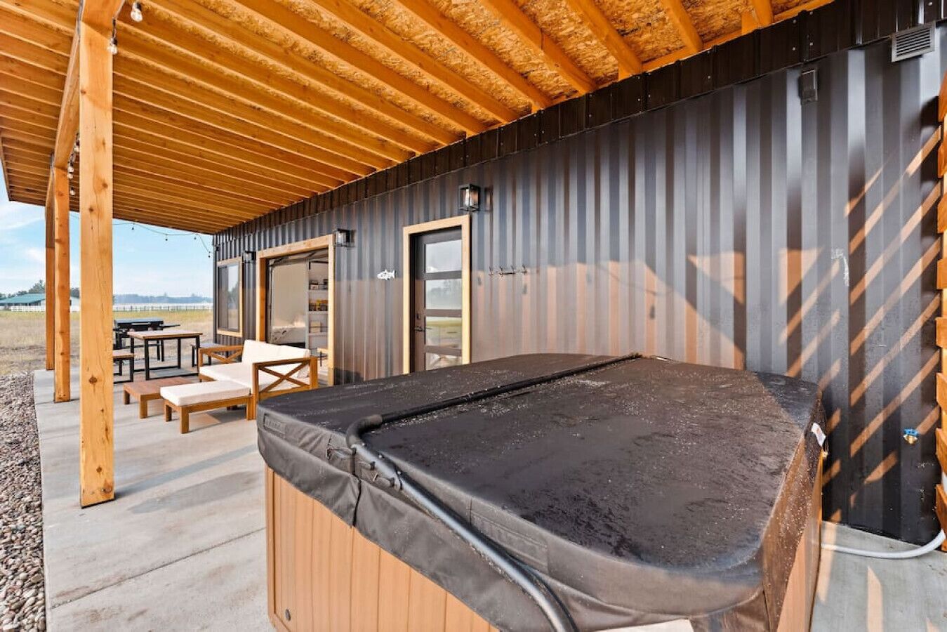 A pool table under a wooden roof with outdoor seating and a view of the countryside.
