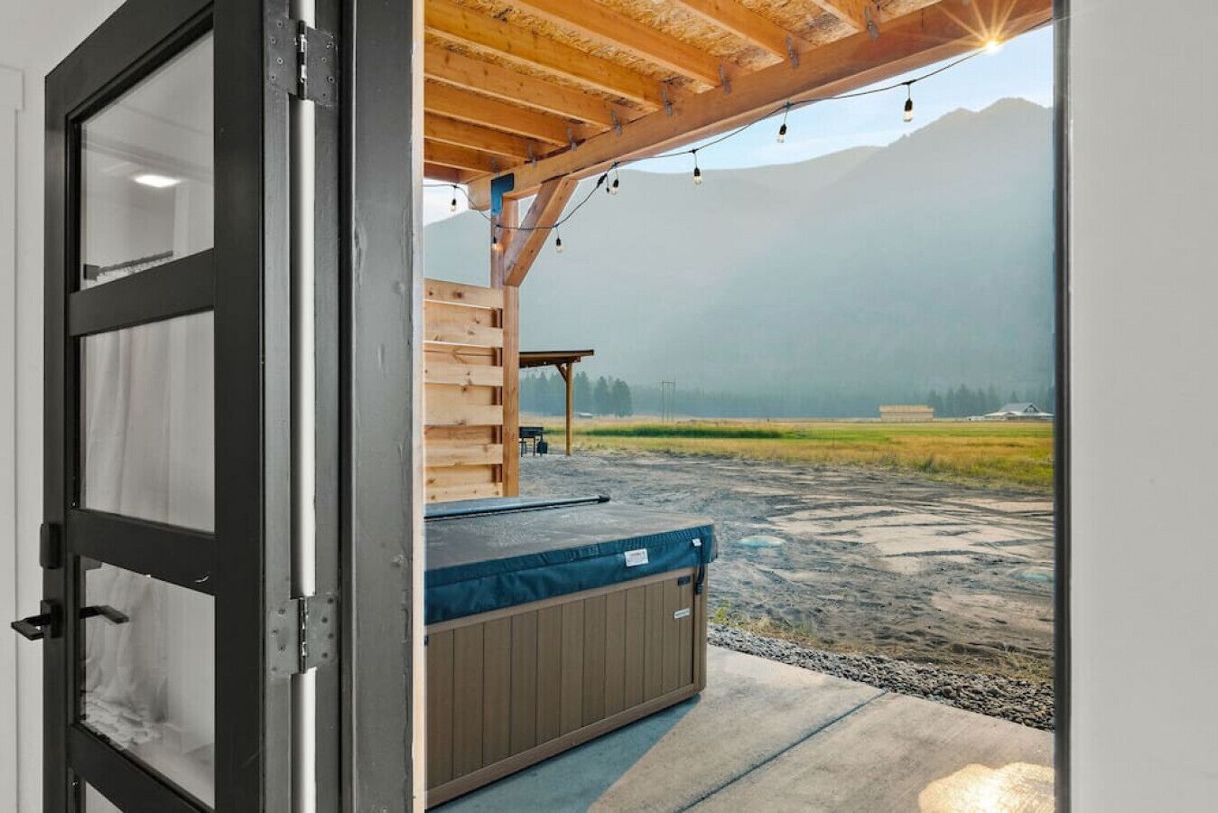 A room with a large sliding door leading to an outdoor area with a hot tub, wooden deck, and a view of a mountainous landscape.