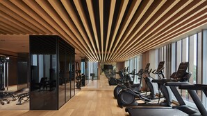 Ein Fitnessraum mit Trainingsgeräten, großen Fenstern und einer Holzbalkendecke.