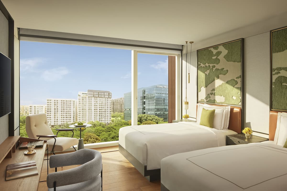 A modern hotel room with a large window, two beds, a desk, and a chair.