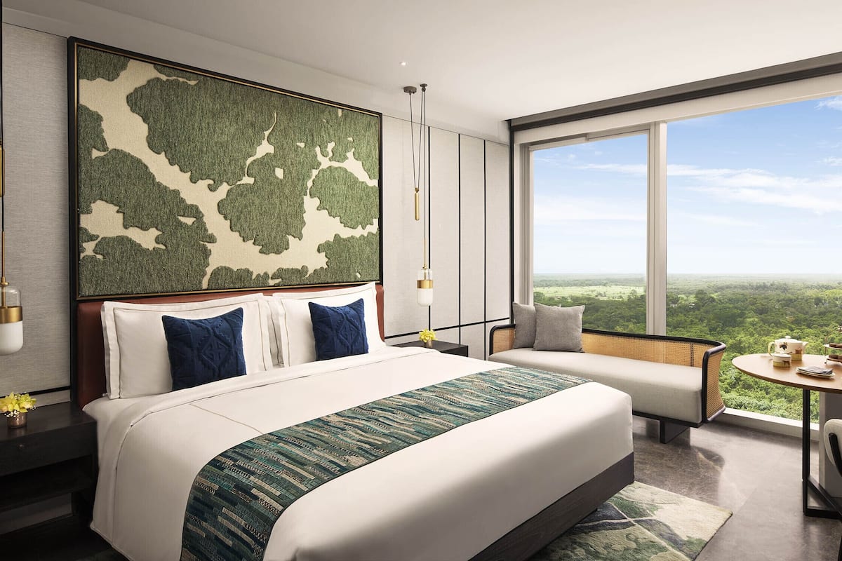 A modern hotel room with a large bed, a seating area with a view, and a small table with tea set.