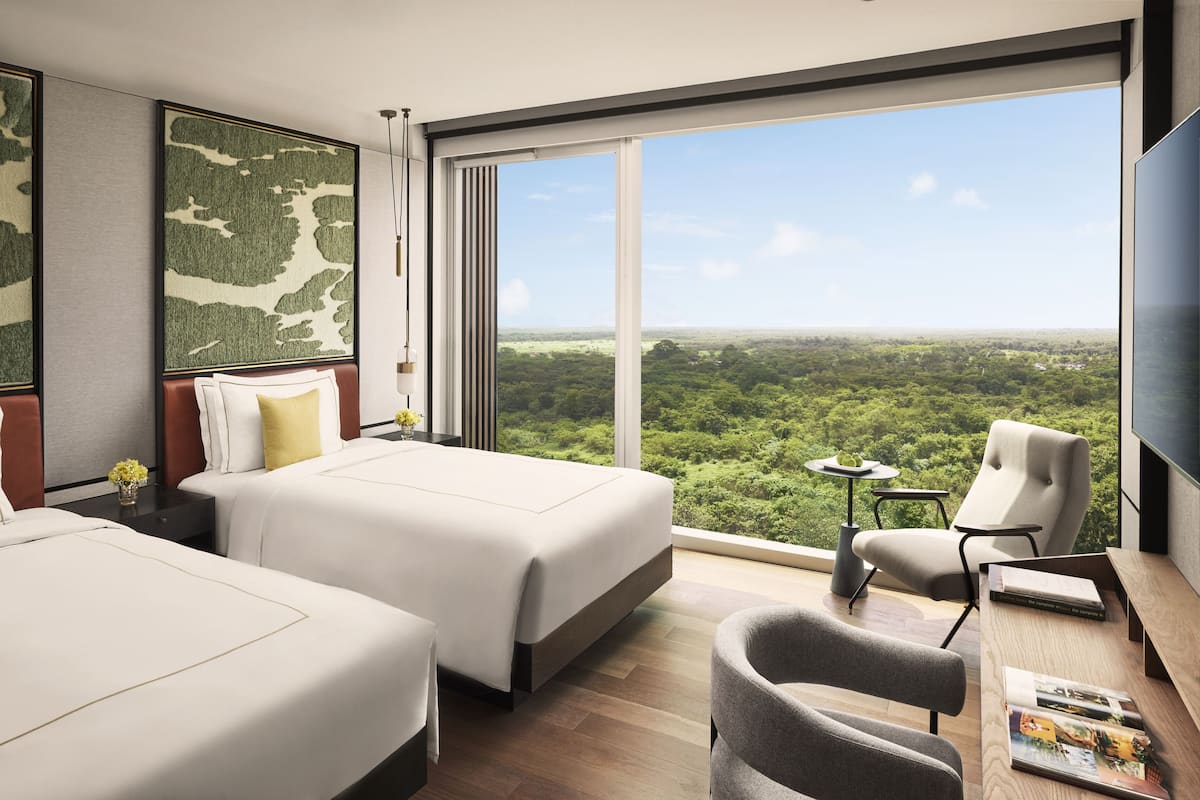 A hotel room with two beds, a large window with a city view, a desk with a chair, and a TV.