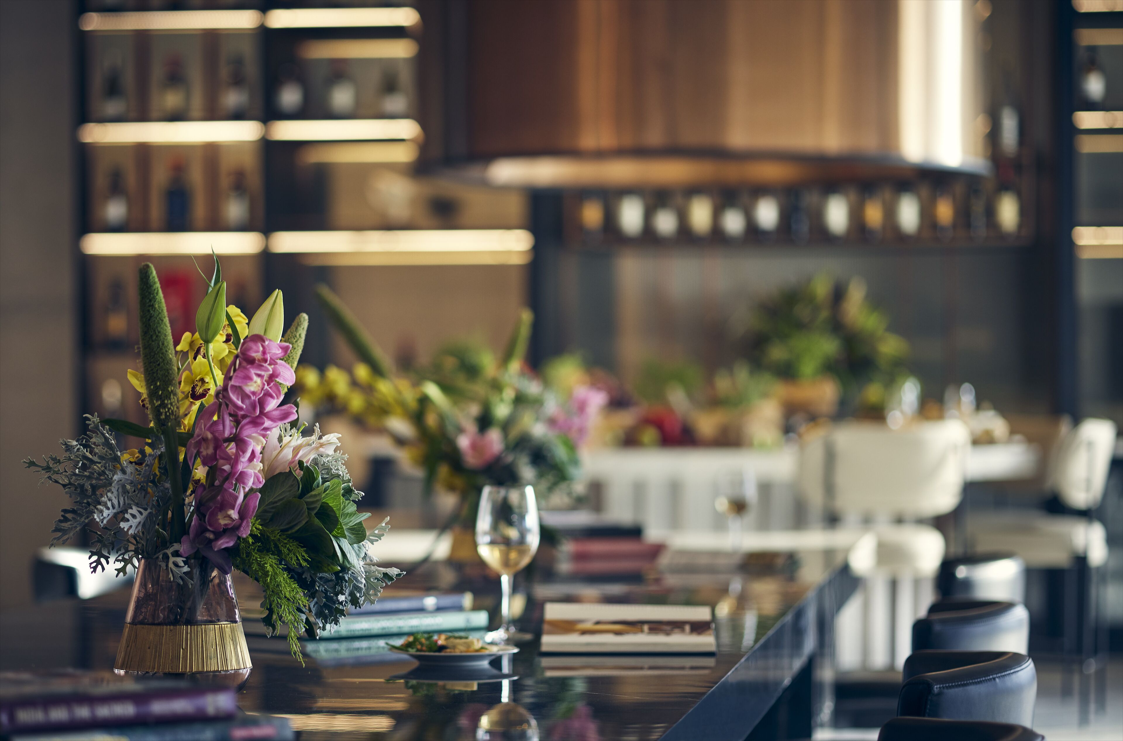 A dining area with a table set for two, featuring a vase of flowers and a wine glass.