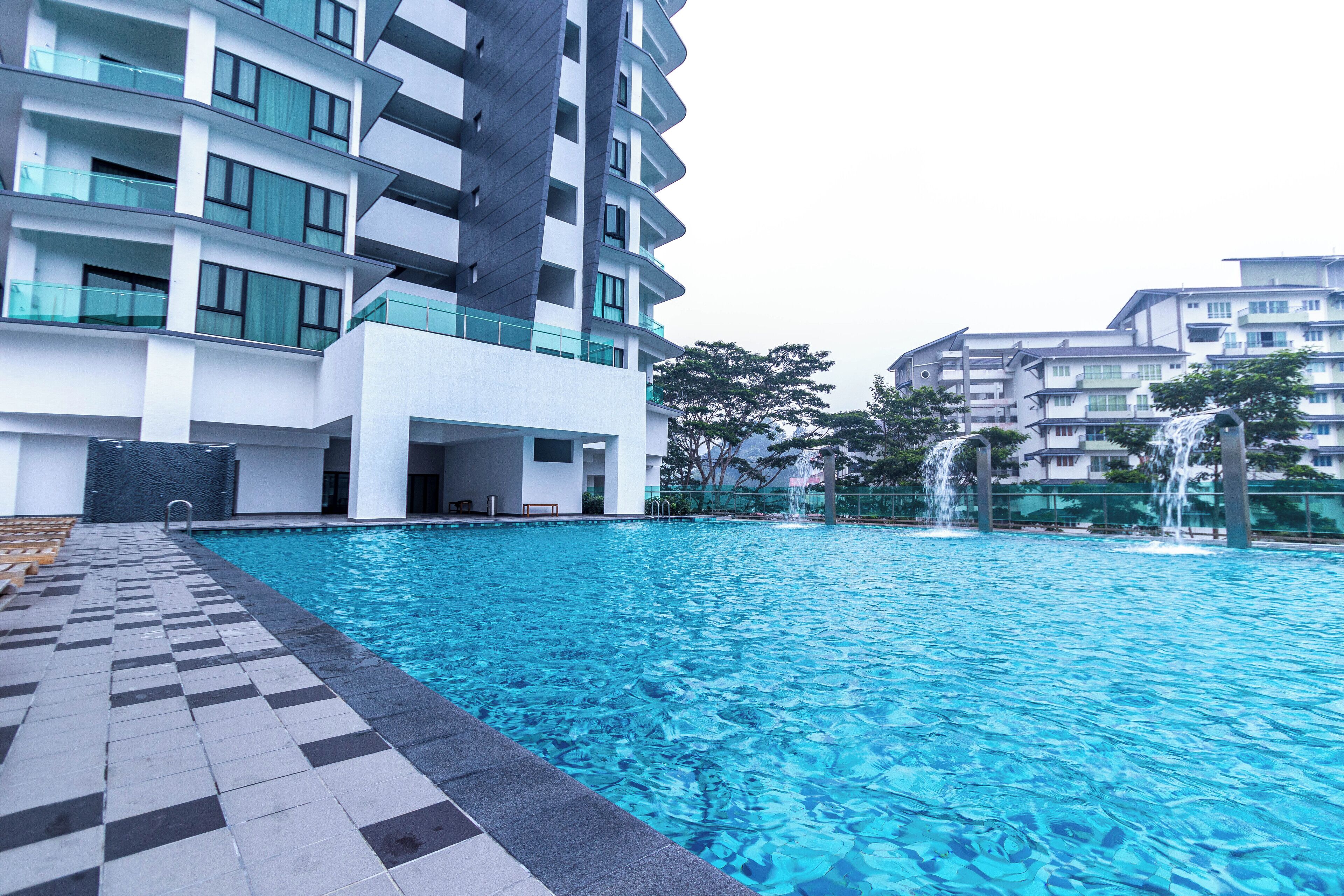 A modern swimming pool area with a checkered tile pattern, surrounded by multi-story residential buildings with balconies and large windows.