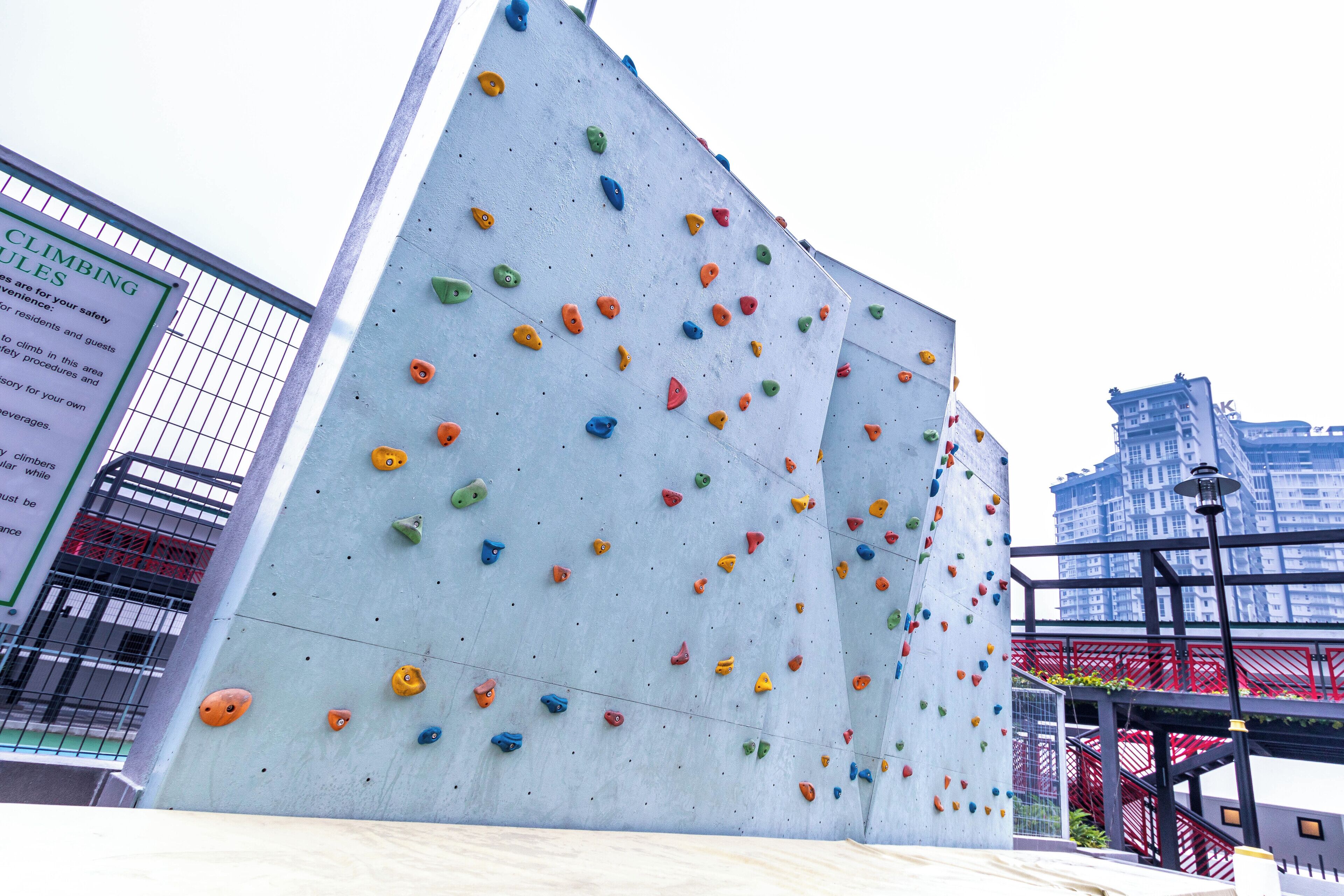 A climbing wall with various colored holds, a metal fence, and a sign with climbing rules.