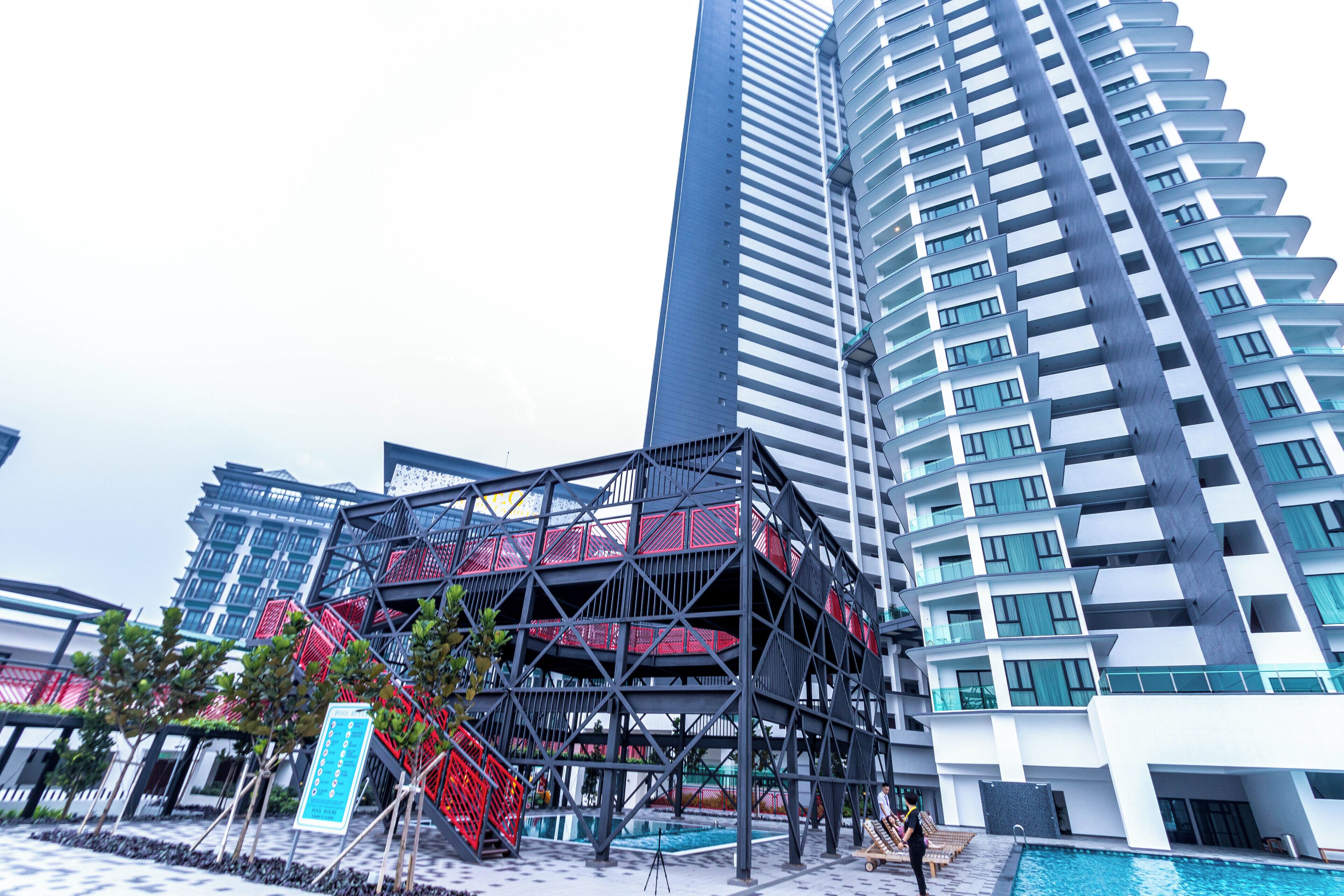 Un immeuble moderne de grande hauteur, avec une structure distinctive aux couleurs rouge et noire, visible au premier plan. Il s’agit probablement d’un espace public ou d’une entrée.