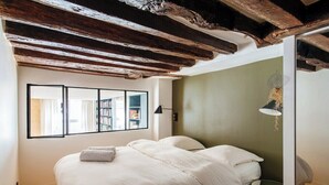 Un dormitorio con una cama grande, vigas de madera en el techo, una estantería y una ventana con vistas al exterior.