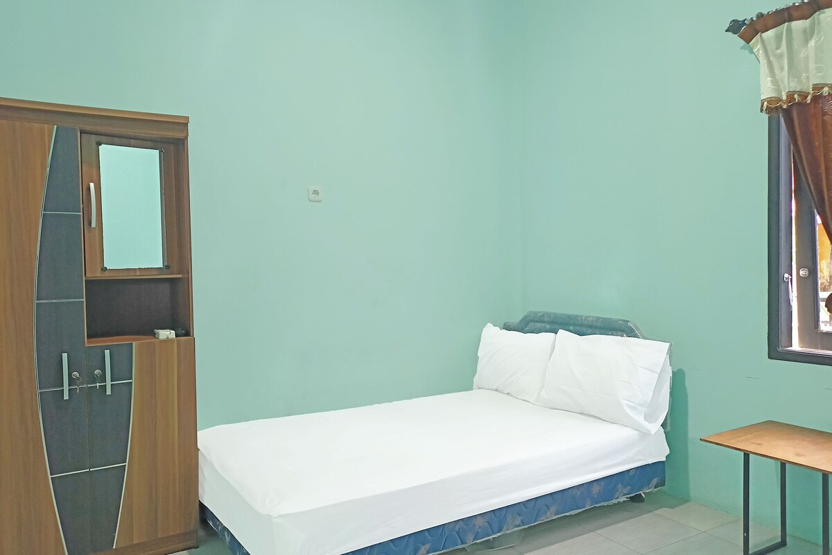 A room with a bed, a wooden wardrobe, a small table, and a window with curtains.