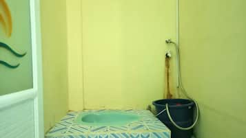 A small bathroom with a blue and white patterned toilet, a blue bucket, and a shower hose.