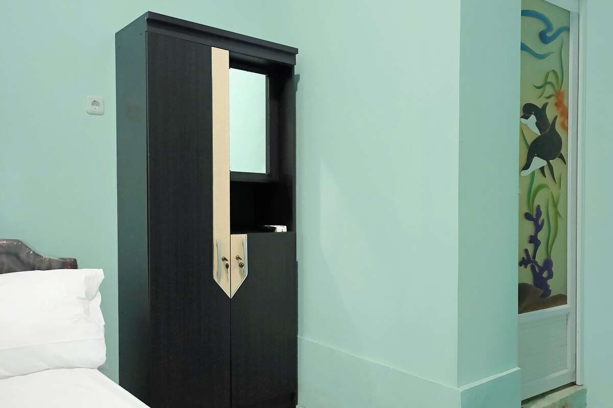 A room with a bed, a dark-colored wardrobe with a mirror, and a door with a colorful mural.