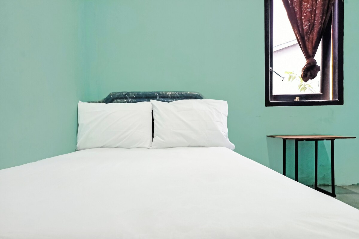 A bed with white bedding, a teal wall, and a small table with a black frame.