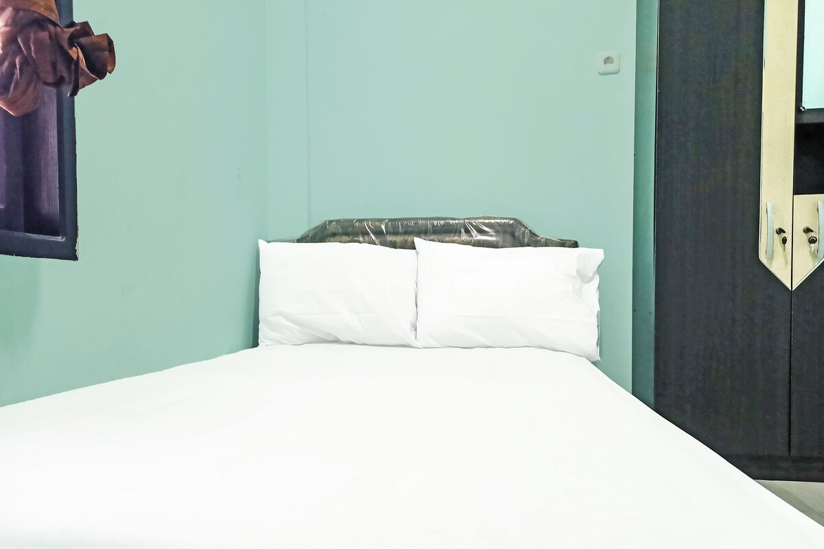 Una cama con ropa blanca, una almohada y un objeto envuelto en plástico sobre el cabecero.
