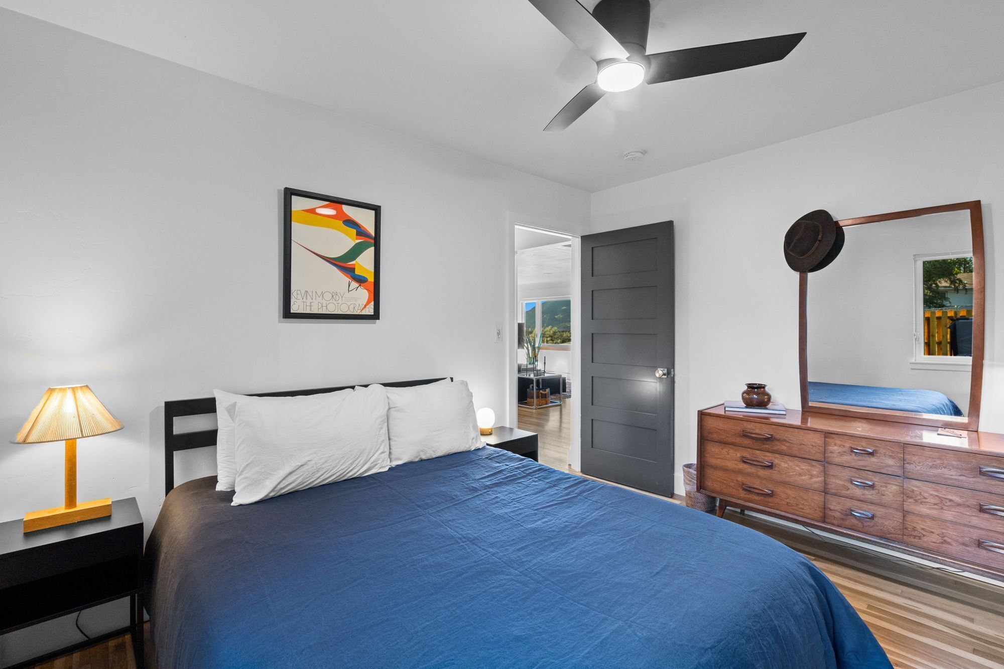 Une chambre à coucher avec un lit, une commode, une lampe, un ventilateur de plafond et un tableau encadré accroché au mur.