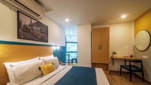 Une chambre d’hôtel avec un lit, un bureau, une chaise, une fenêtre et un tableau au mur.