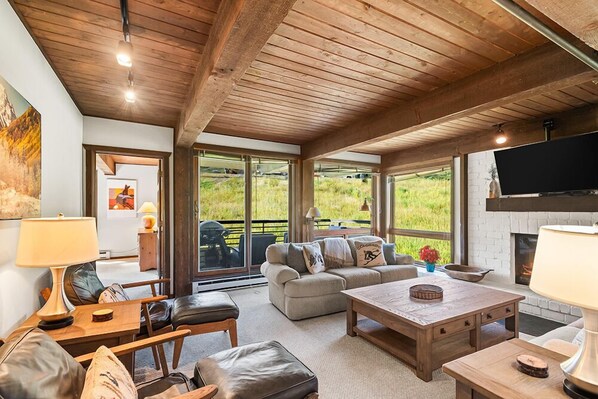 A cozy living room with a fireplace, comfortable seating, and large windows offering a view of the outdoors. - Enclave 208 | Snowmass Ski-In/Ski-Out Condo w/Shared Pool/Hot Tub/WiFi (Snowmass Village)