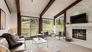 Ein geräumiges Wohnzimmer mit Kamin, großem Fernseher und einem Balkon mit Sitzgelegenheit.