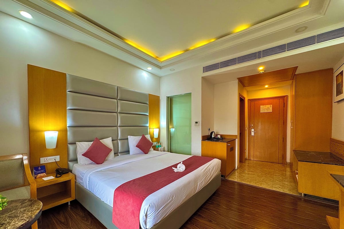 A hotel room with a large bed, bedside tables, a desk, and a door.
