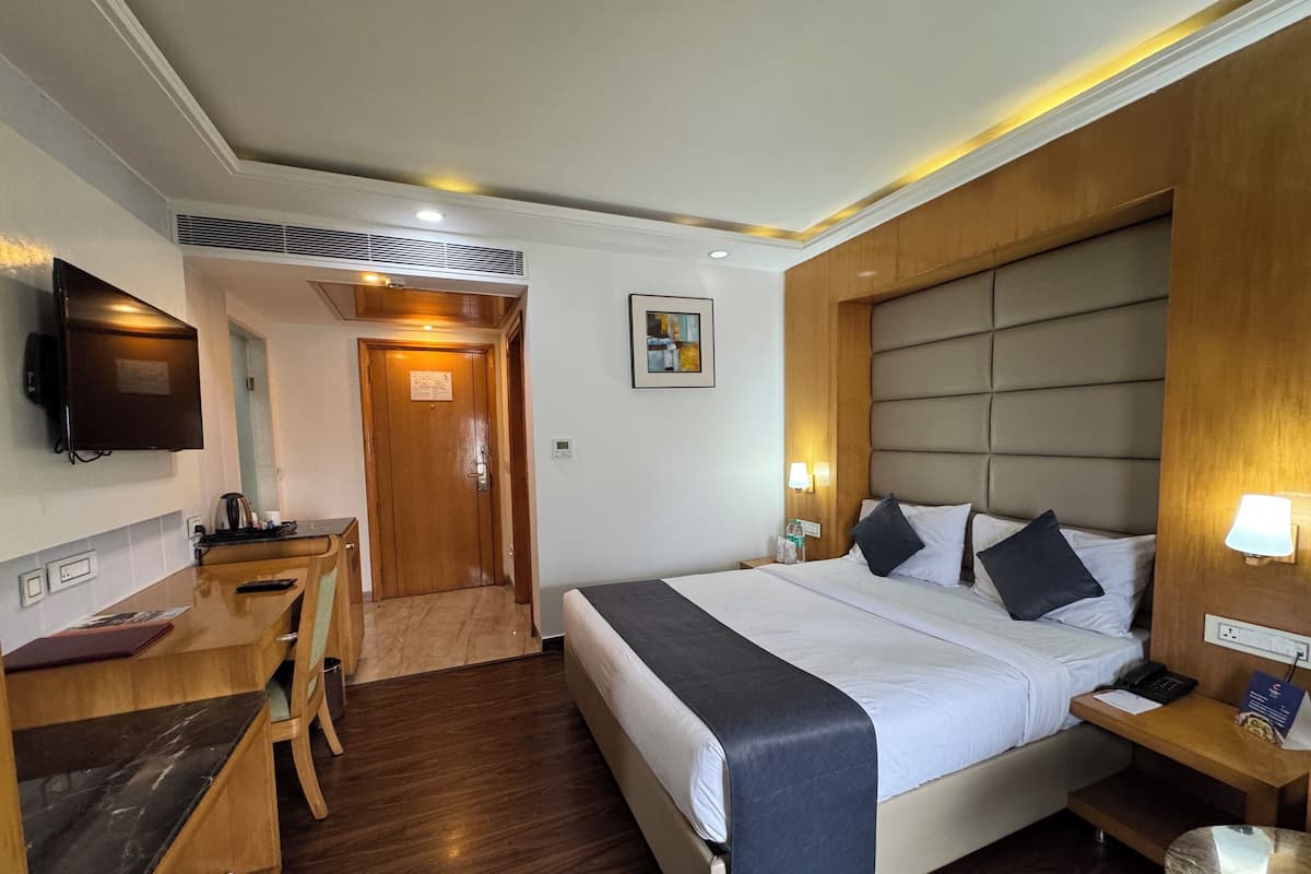 A hotel room with a bed, bedside table, lamp, and a desk with a chair.