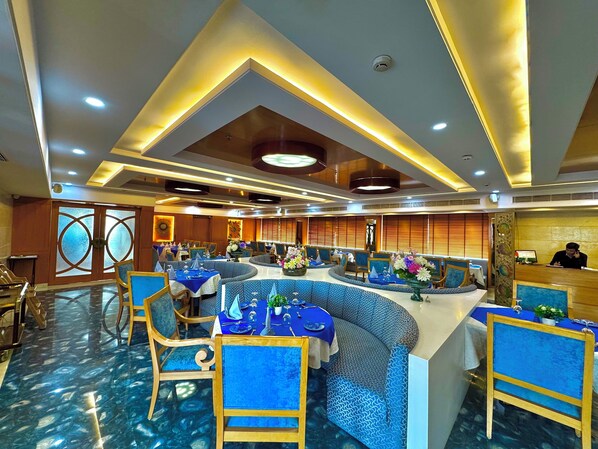 A restaurant with a modern interior, featuring blue seating, a central island, and a wooden reception desk.