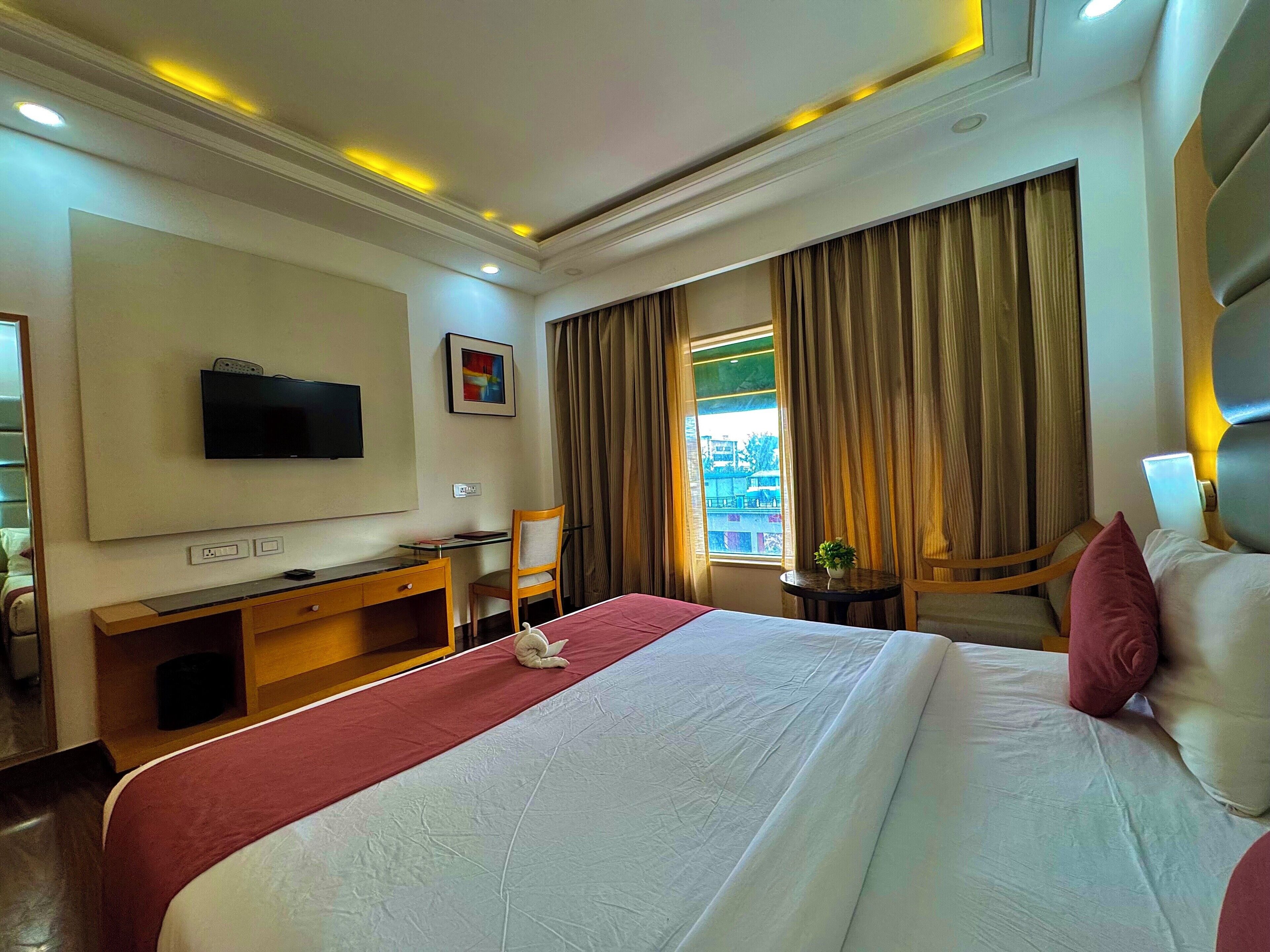 A hotel room with a large bed, a desk with a chair, a television, and a window with curtains.