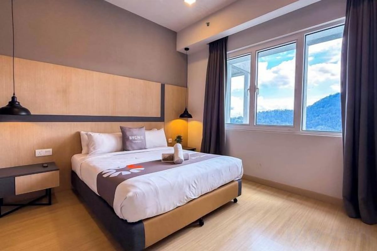 A hotel room with a bed, bedside tables, a window with curtains, and a view of the outdoors.