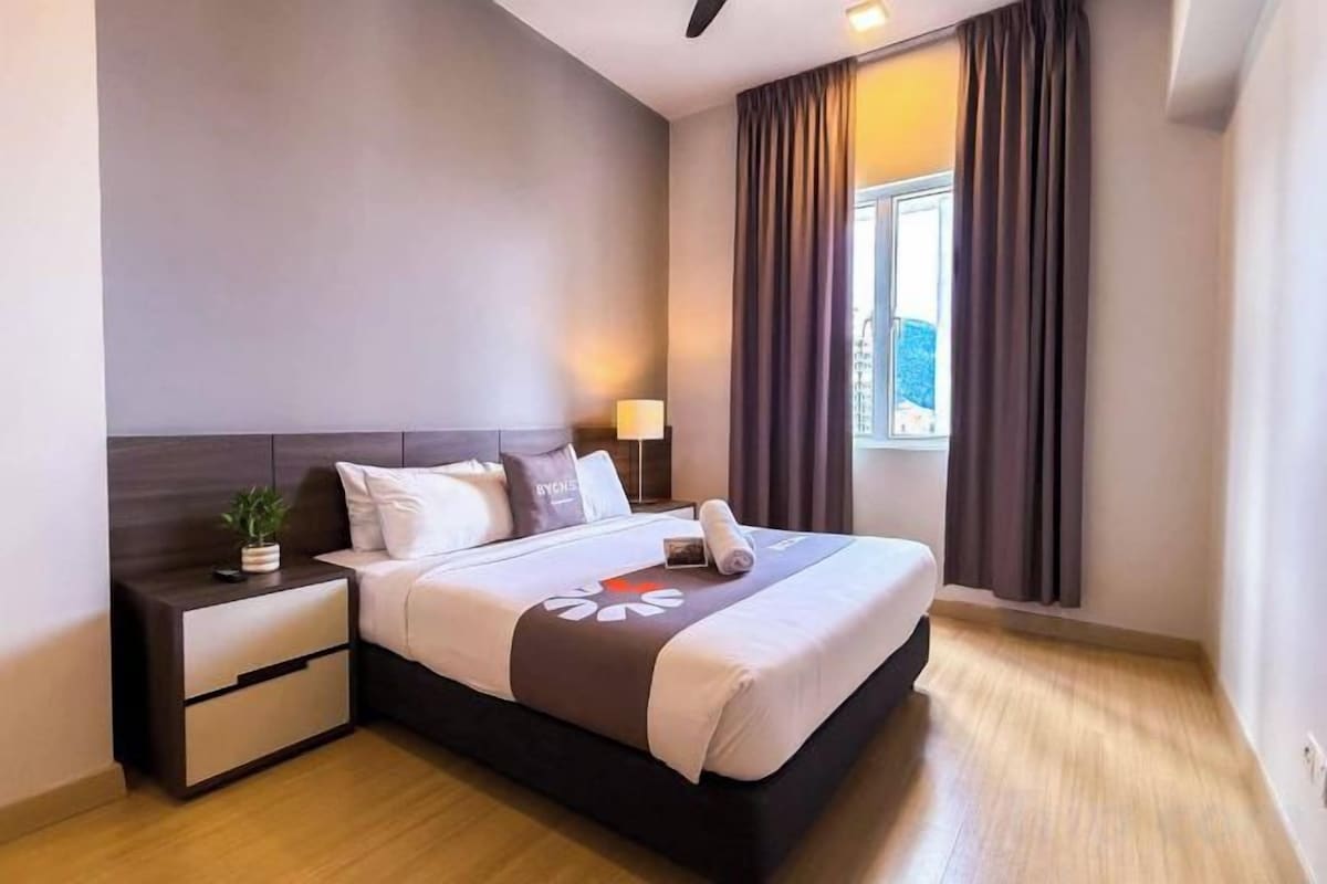 A hotel room with a bed, bedside table, lamp, and a window with curtains.