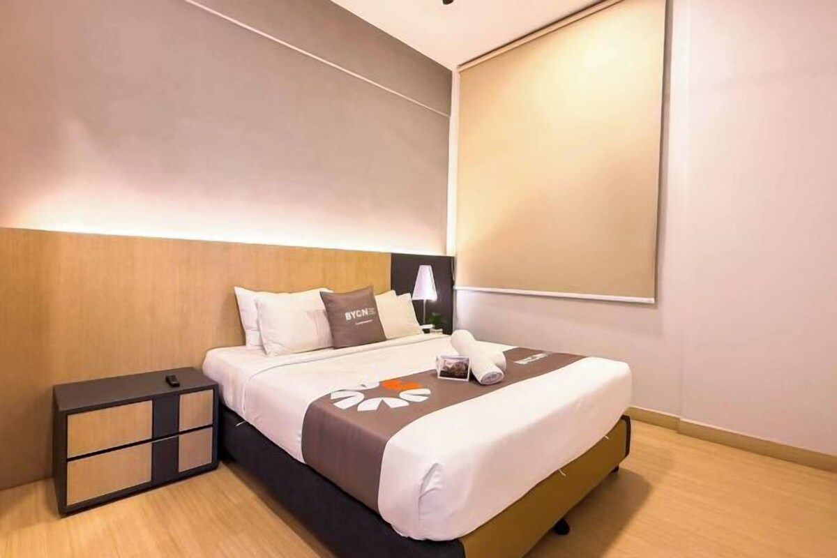A hotel room with a bed, bedside table, lamp, and a large window.