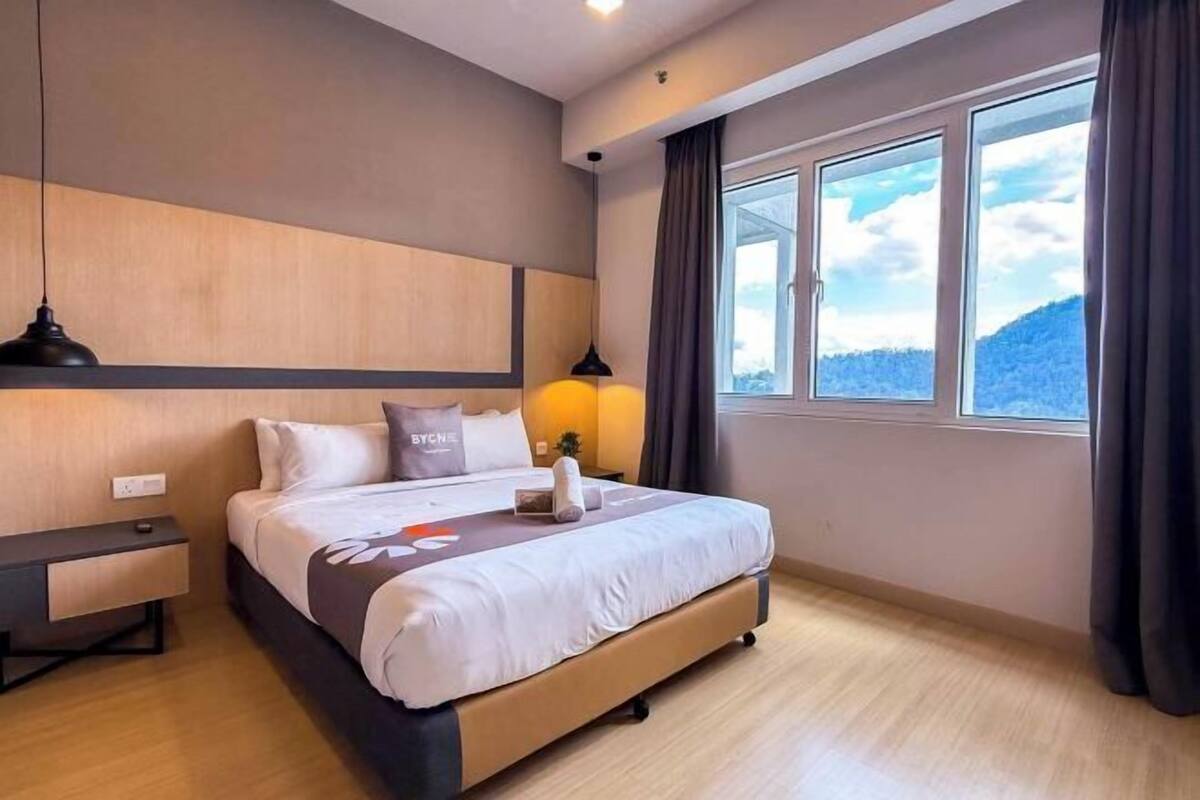 A hotel room with a bed, bedside tables, a window with curtains, and a view of the outdoors.