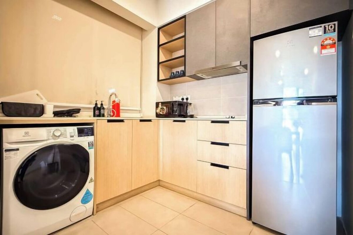 A compact kitchen with a washing machine, a refrigerator, and wooden cabinets.