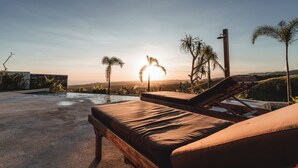 Ein Liegebereich am Pool mit Blick auf den Sonnenuntergang und Palmen.