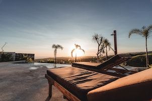 Zona de descanso junto a la piscina con vista al atardecer y palmeras.