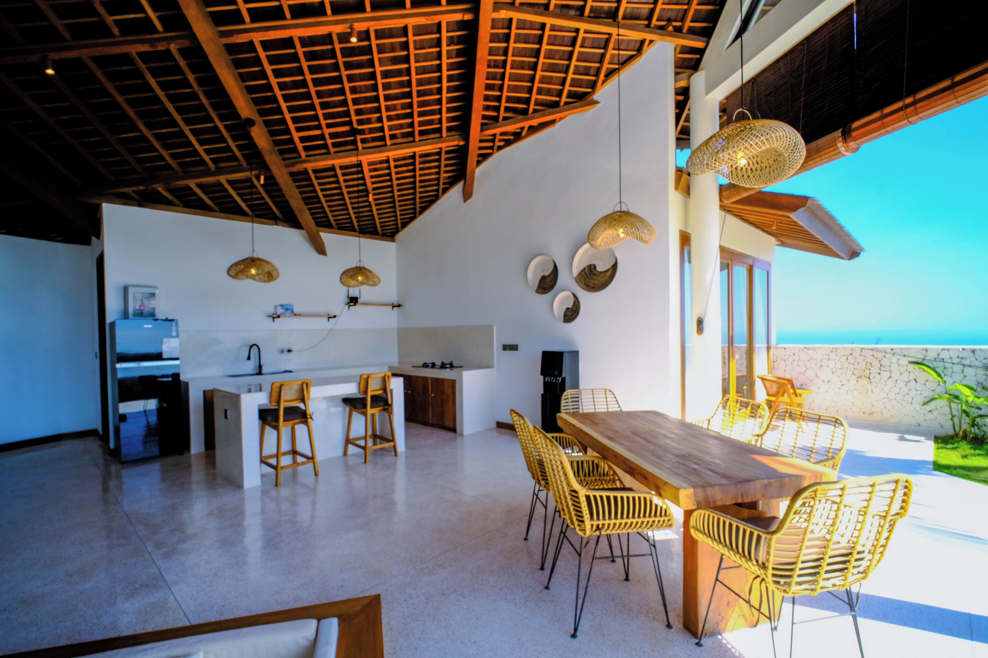Una cocina moderna con techo de madera, un comedor con sillas amarillas y vistas al océano.