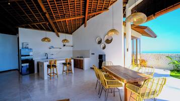 Una cocina moderna con techo de madera, un comedor con sillas amarillas y vistas al océano.